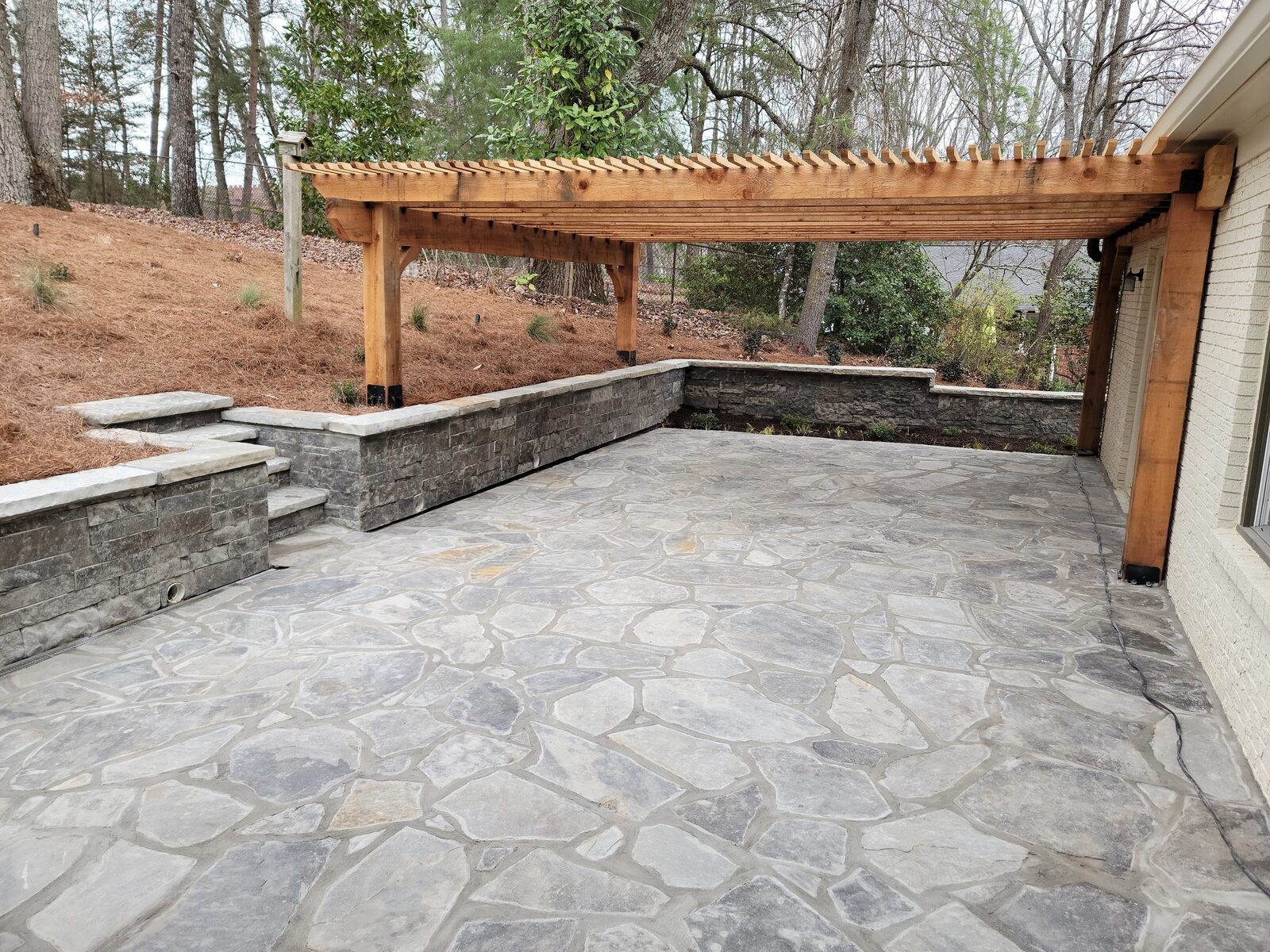 Paver patio with a cedar pergola and built-in stone seating